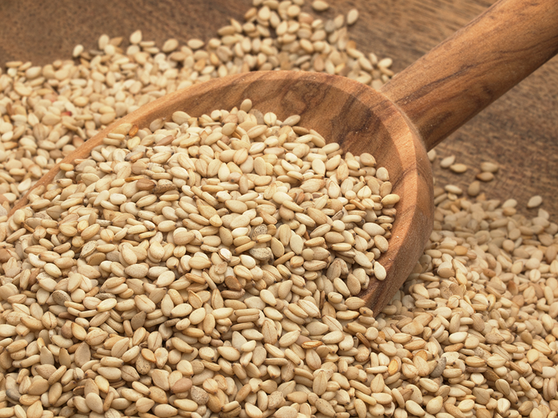 Sesame seeds being scooped up by a wooden spoon.