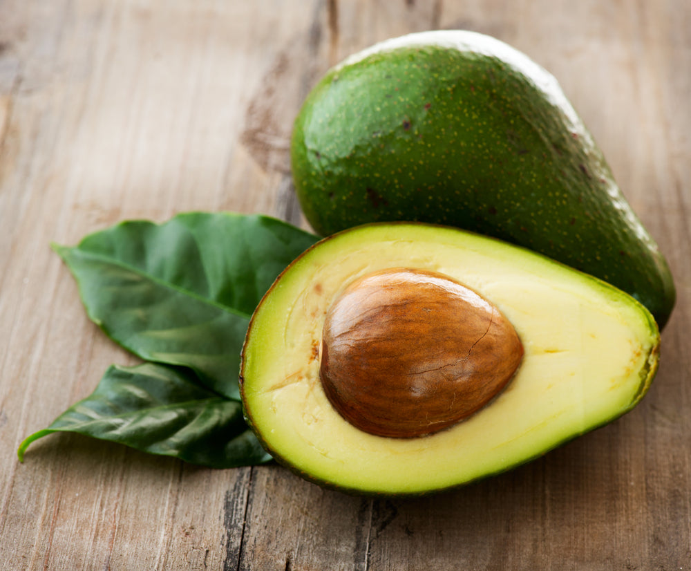 1 avocado and an avocado sliced in half showing its big seed which can be grown into it's plant. Avocado is a super food and a very healthy fat alternative.