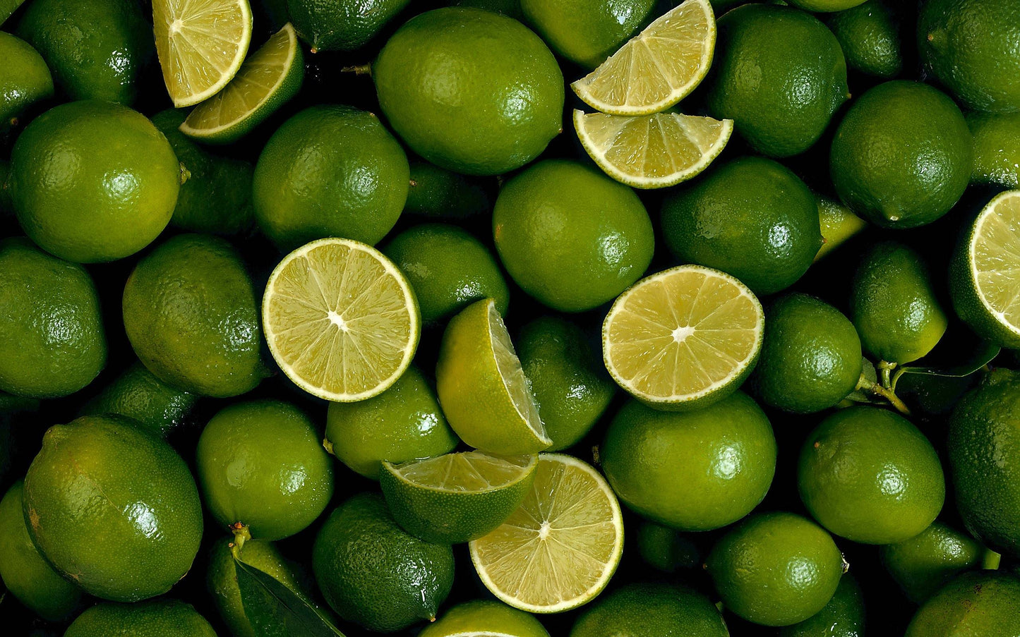 Lots of limes with some cut into wedges showing of the juicy centre of the citrus fruit.