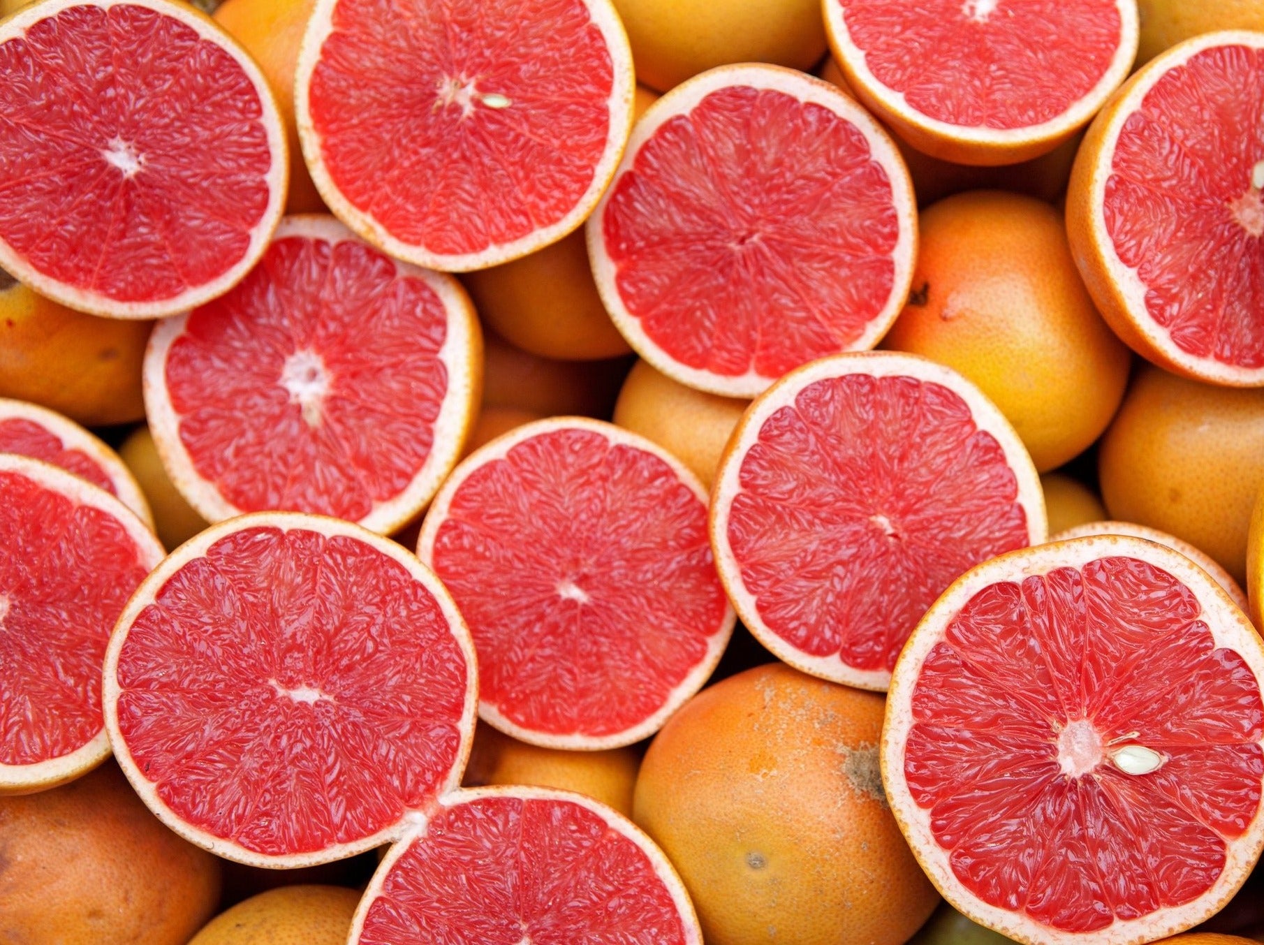 Many grapefruits with some cut in half to show off the fruity centre that people consume as a delicious snack or juice to create oils for its many other uses.